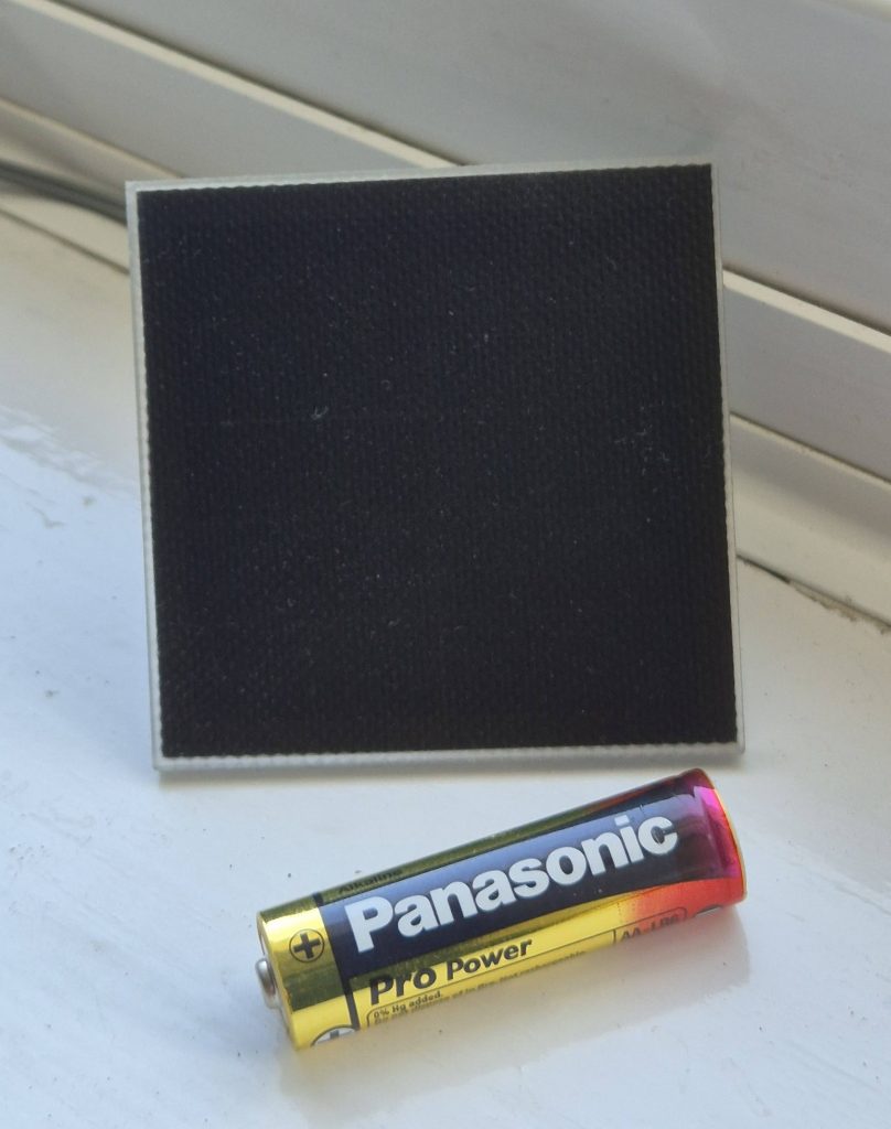 Picture shows a small solar panel from the Voltaic range with a AA battery just in front to provide a familiar reference of scale. The solar panel is square and the length of each side is about 1cm longer than the length of the AA battery.
