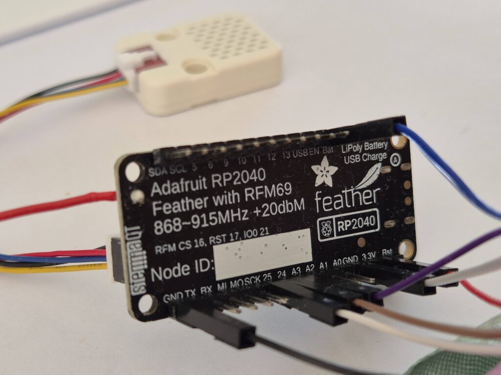 Photo of Adafruit Feather RP2040 RFM69 with an ENV sensor in the background